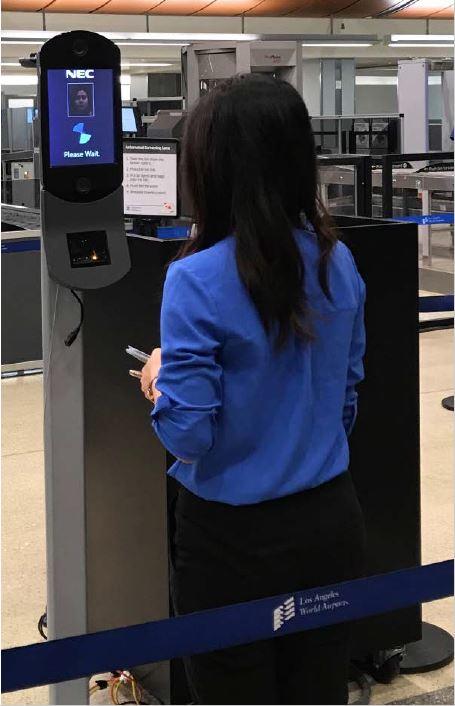An example of a face recognition kiosk from TSA's website. A woman stands facing a small screen that's about five feet off the ground on a pedestal. This is an example of a face recognition kiosk from TSA's website.